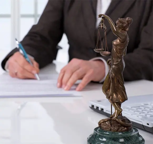 A person sitting at a desk with papers and a statue of justice.