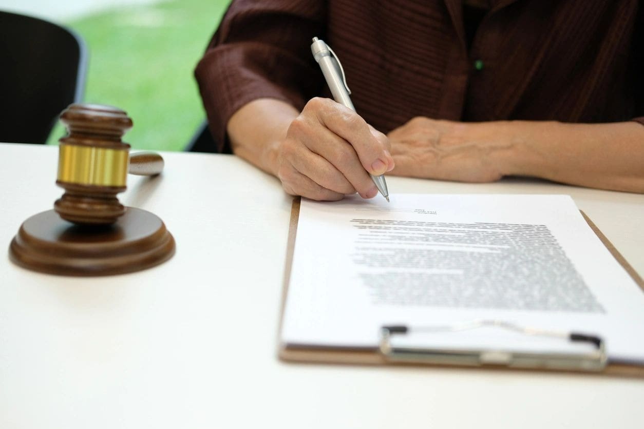 A person signing papers on top of a table.