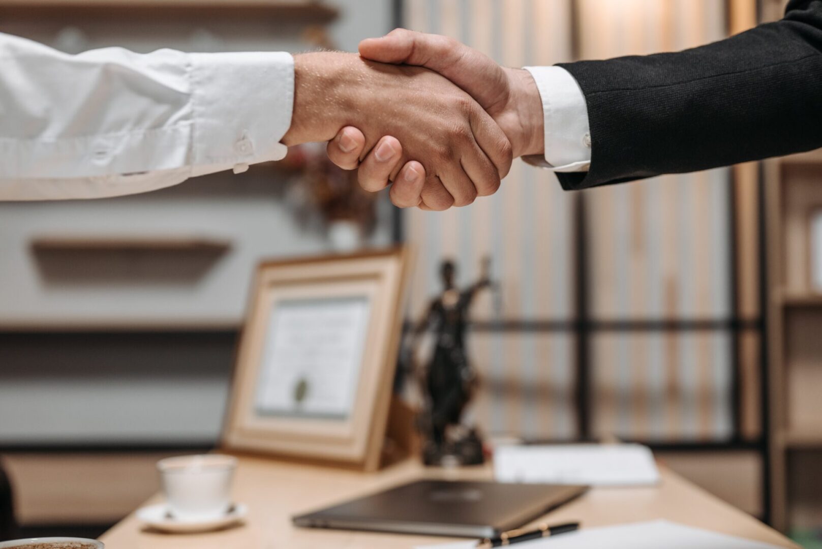 Two people shaking hands over a desk.